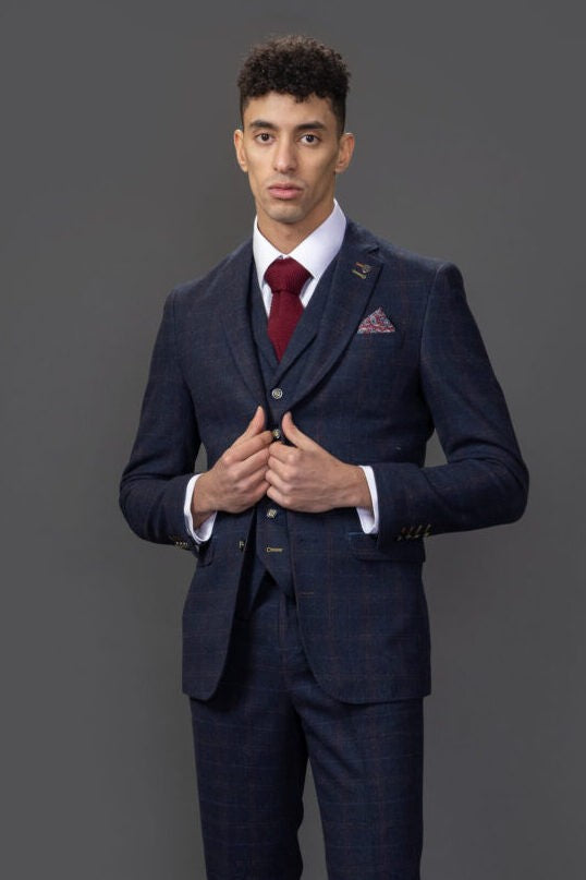 Man wearing a navy suit with a red tie and pocket square on a gray background