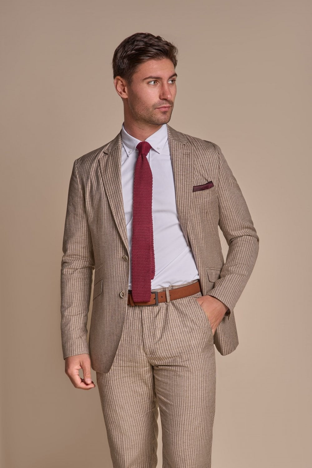 Man wearing a beige suit with a red tie and pocket square against a beige background