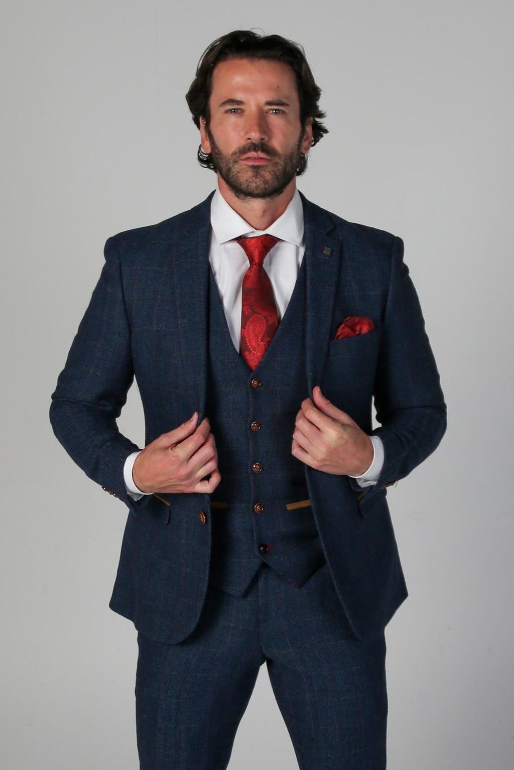 Man wearing a blue suit with a red tie and pocket square on a gray background