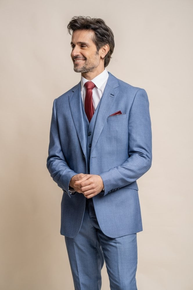 Man wearing a light blue suit with a red tie and pocket square on a beige background