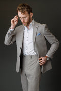 Man wearing a gray suit with a white shirt and blue pocket square against a dark background