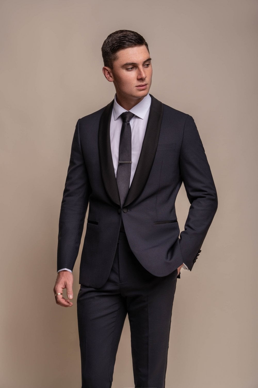 Man wearing a black suit with a white shirt and gray tie against a beige background