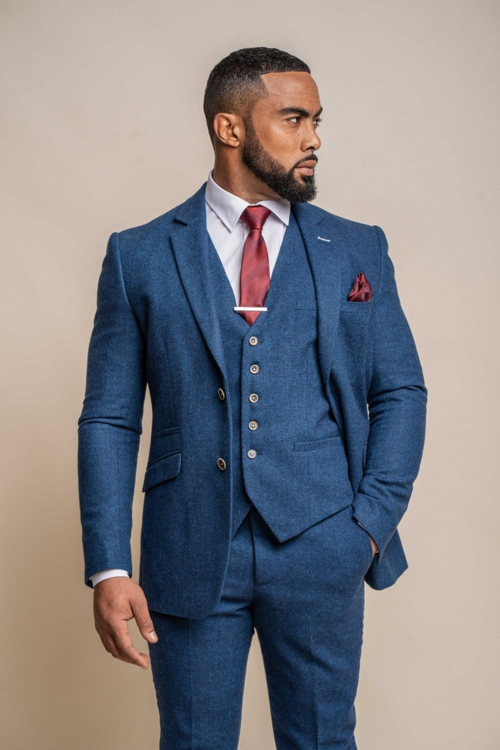 Man wearing a blue suit with a red tie and pocket square against a beige background