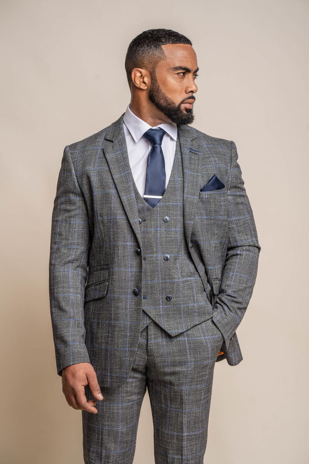 Man wearing a gray checkered suit with a blue tie and pocket square on a beige background