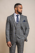 Man wearing a gray checkered suit with a blue tie and pocket square on a beige background