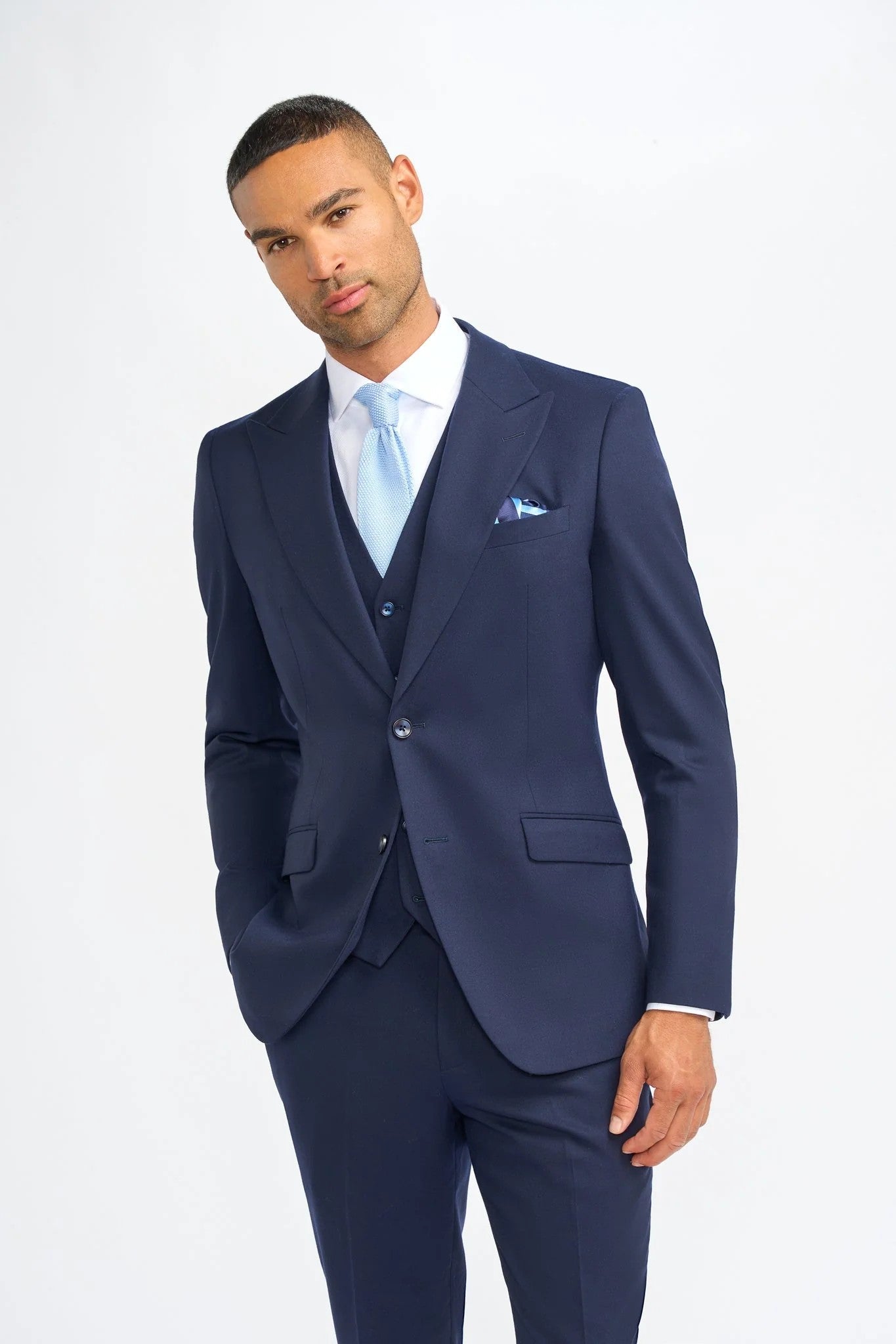 Man wearing a navy suit with a light blue tie and pocket square on a white background