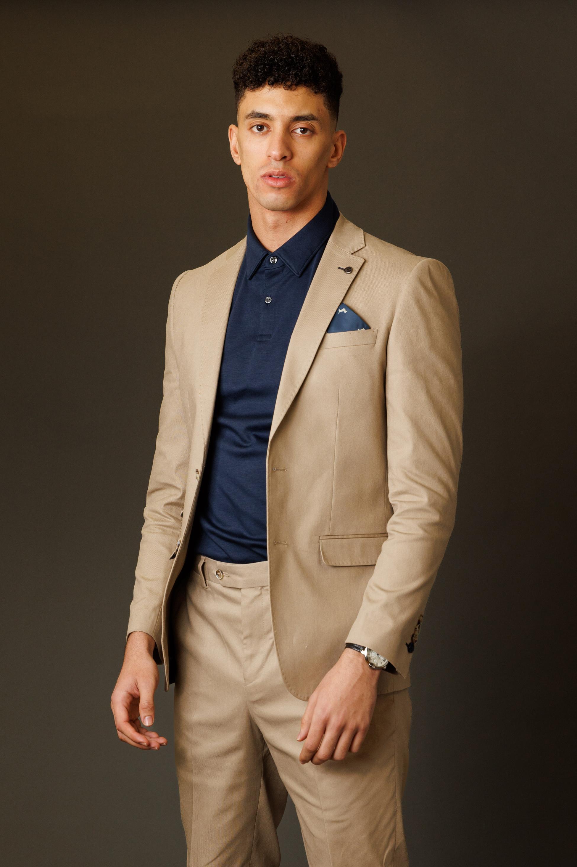 Man wearing a beige suit and navy shirt against a dark background