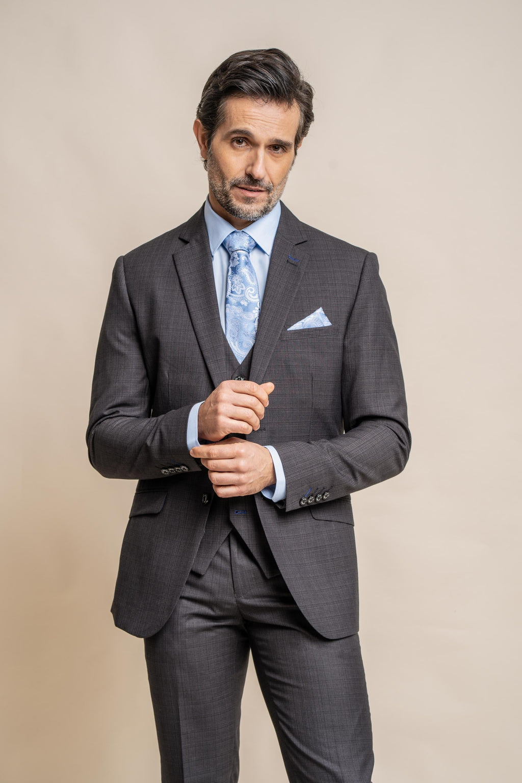 Man wearing a gray suit with a blue tie and pocket square on a beige background