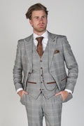 Man wearing a gray checkered suit with a white shirt and brown tie on a light gray background