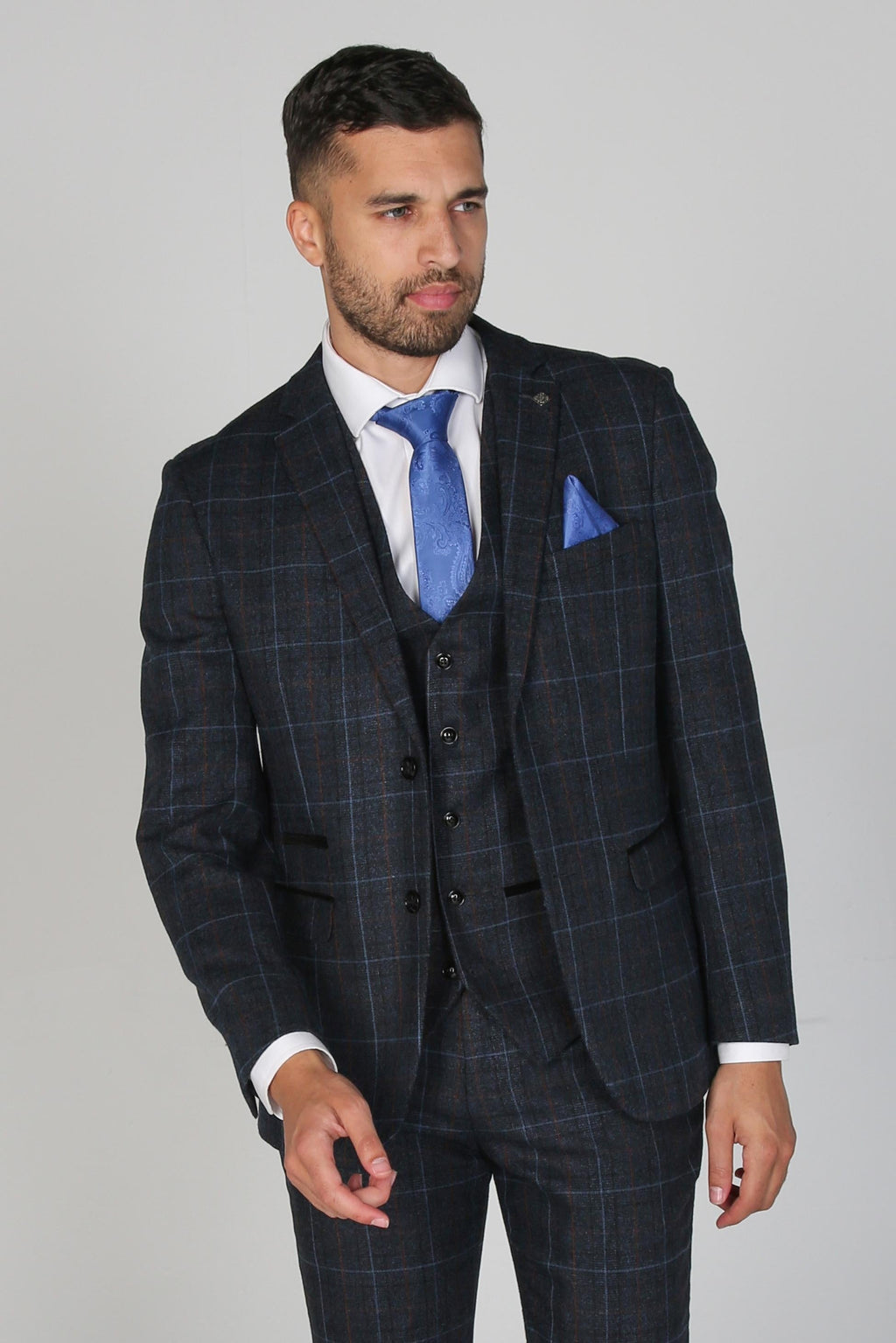 Man wearing a dark checkered suit with a blue tie and pocket square on a gray background