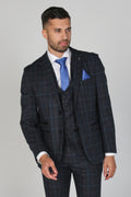 Man wearing a dark checkered suit with a blue tie and pocket square on a gray background