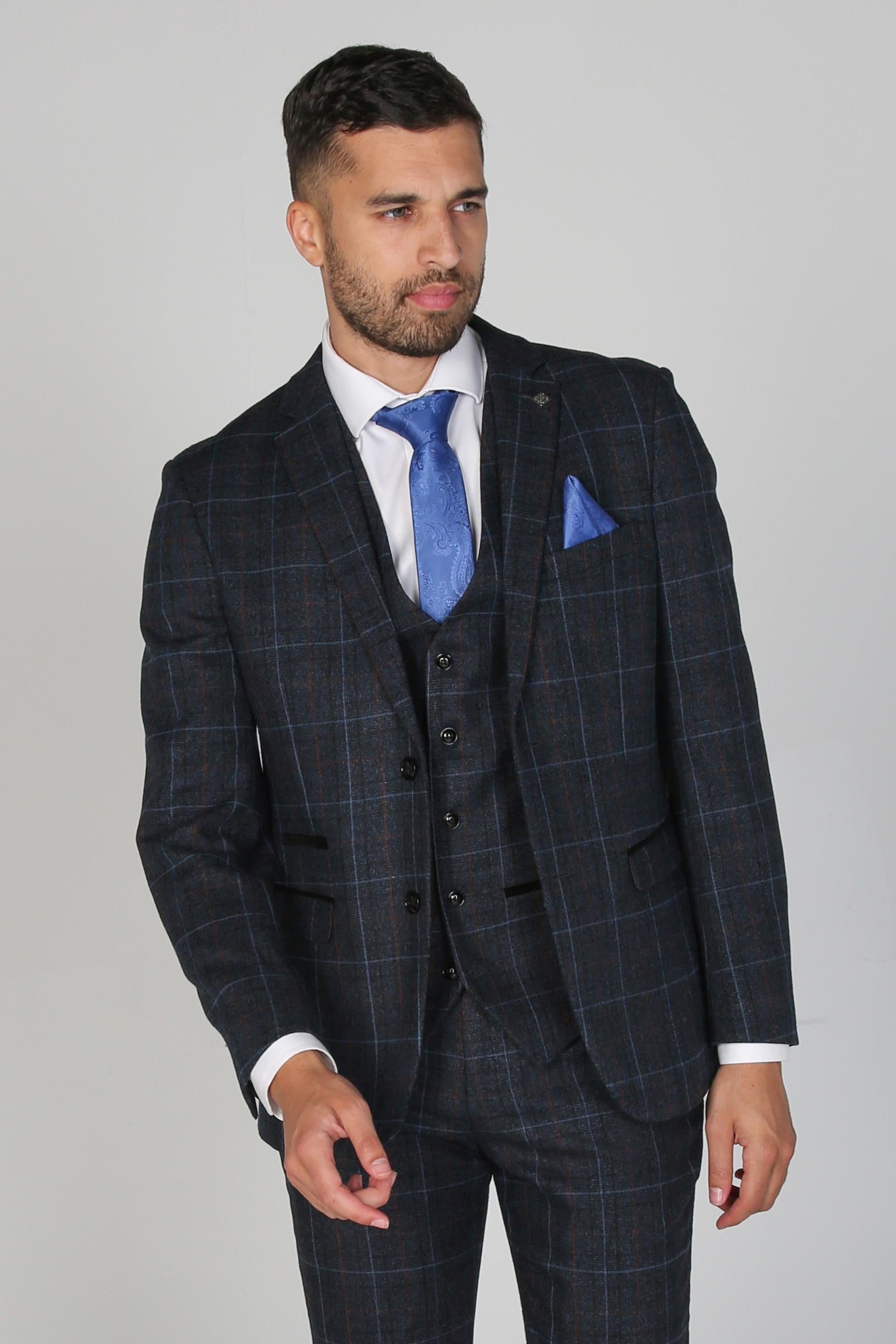 Man wearing a dark checkered suit with a blue tie and pocket square on a gray background