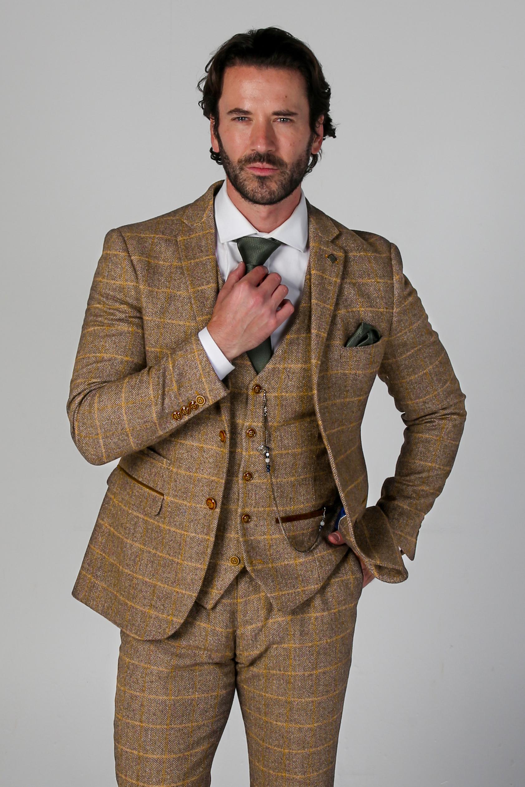 Man wearing a brown checkered suit with a white shirt and green tie on a gray background