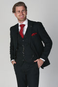 Man wearing a black suit with a red tie and pocket square on a gray background
