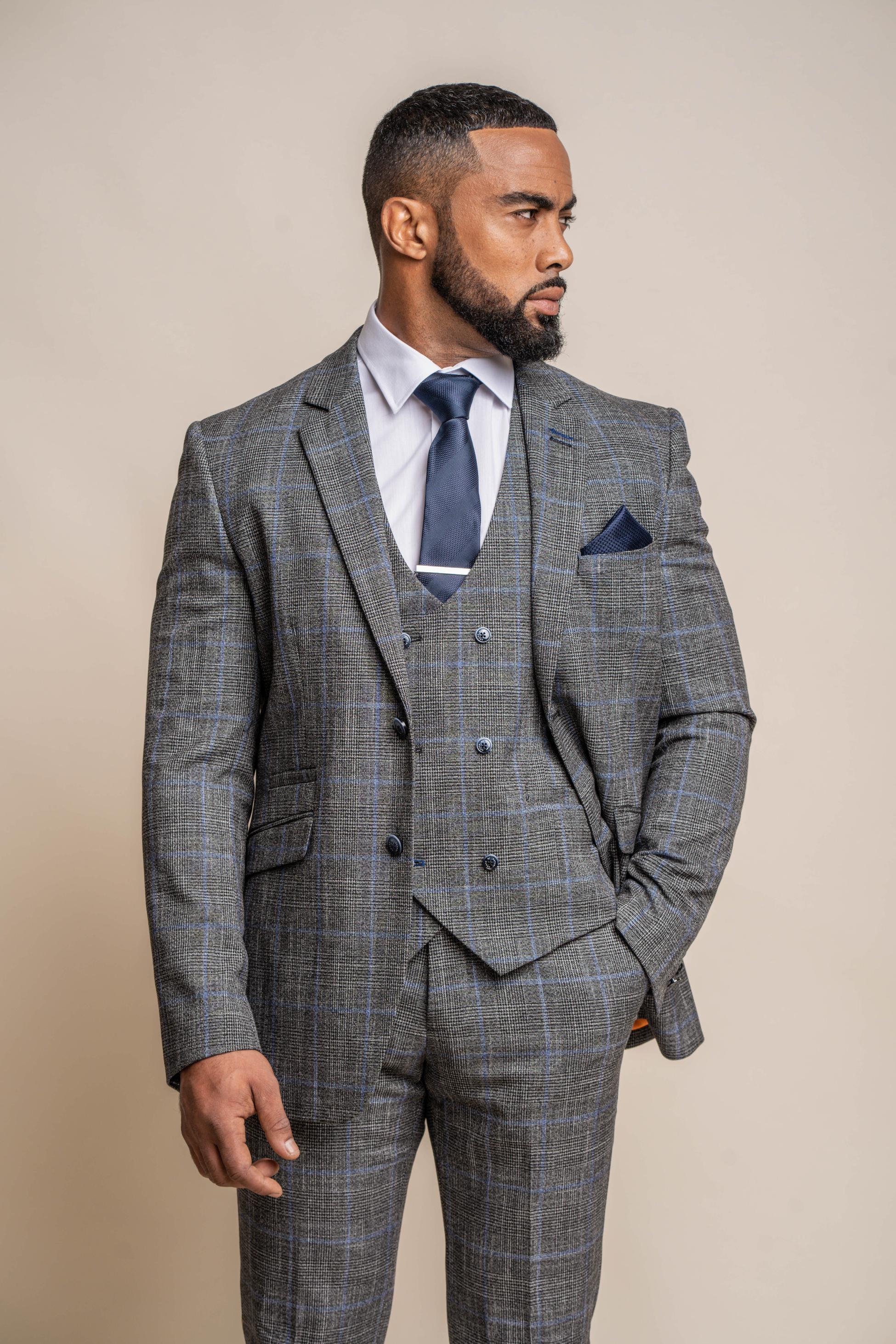 Man wearing a gray checkered suit with a blue tie and pocket square on a beige background