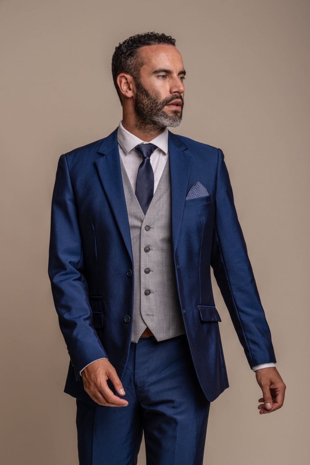 Man wearing a blue suit with a gray vest and tie against a beige background