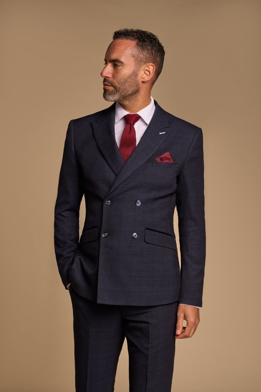 Man wearing a navy suit with a red tie and pocket square on a beige background