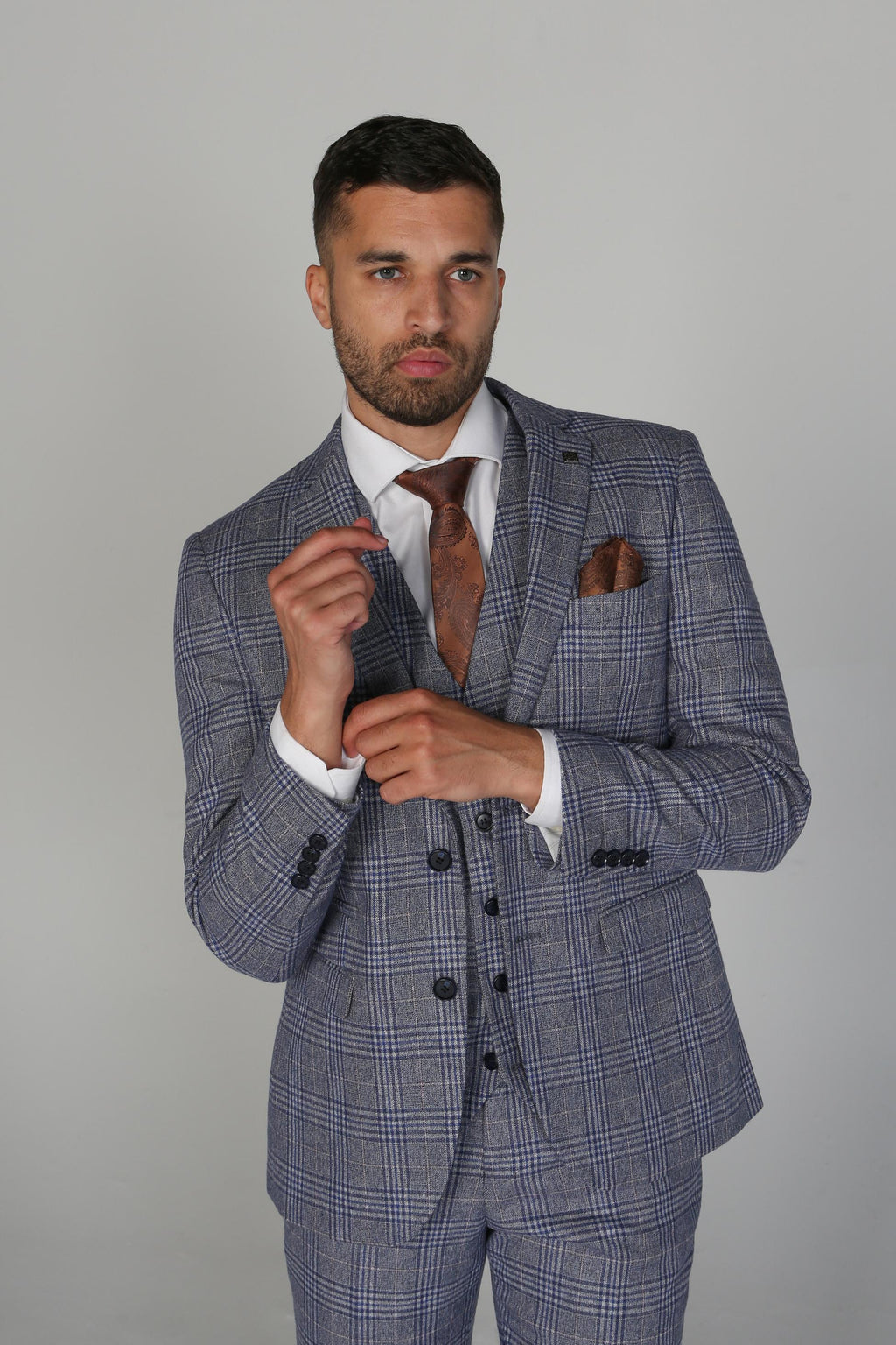Man wearing a gray checkered suit with a brown tie and pocket square on a plain background