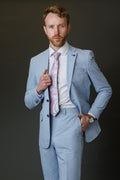 Man adjusting his light blue suit jacket against a dark background