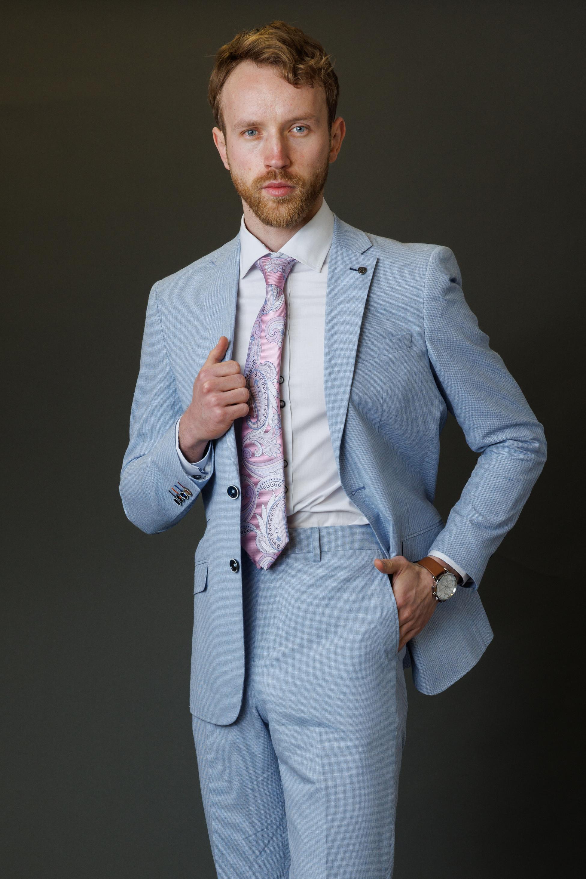 Man adjusting his light blue suit jacket against a dark background