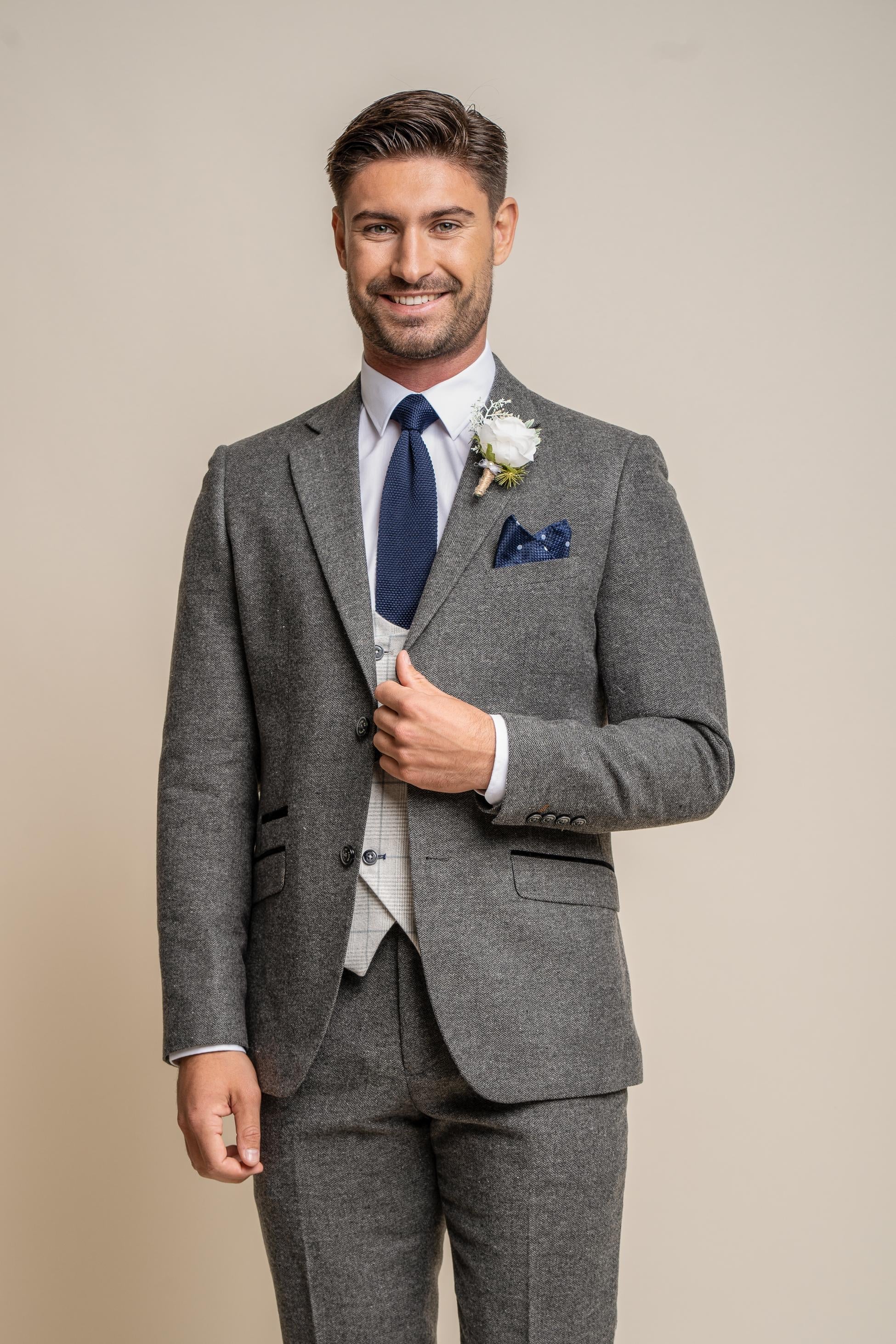 Man wearing a gray suit with a blue tie and pocket square on a beige background