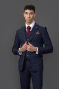 Man wearing a navy suit with a red tie and pocket square on a gray background